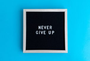 Black letter board with 'Never Give Up' message on a vibrant blue background.
